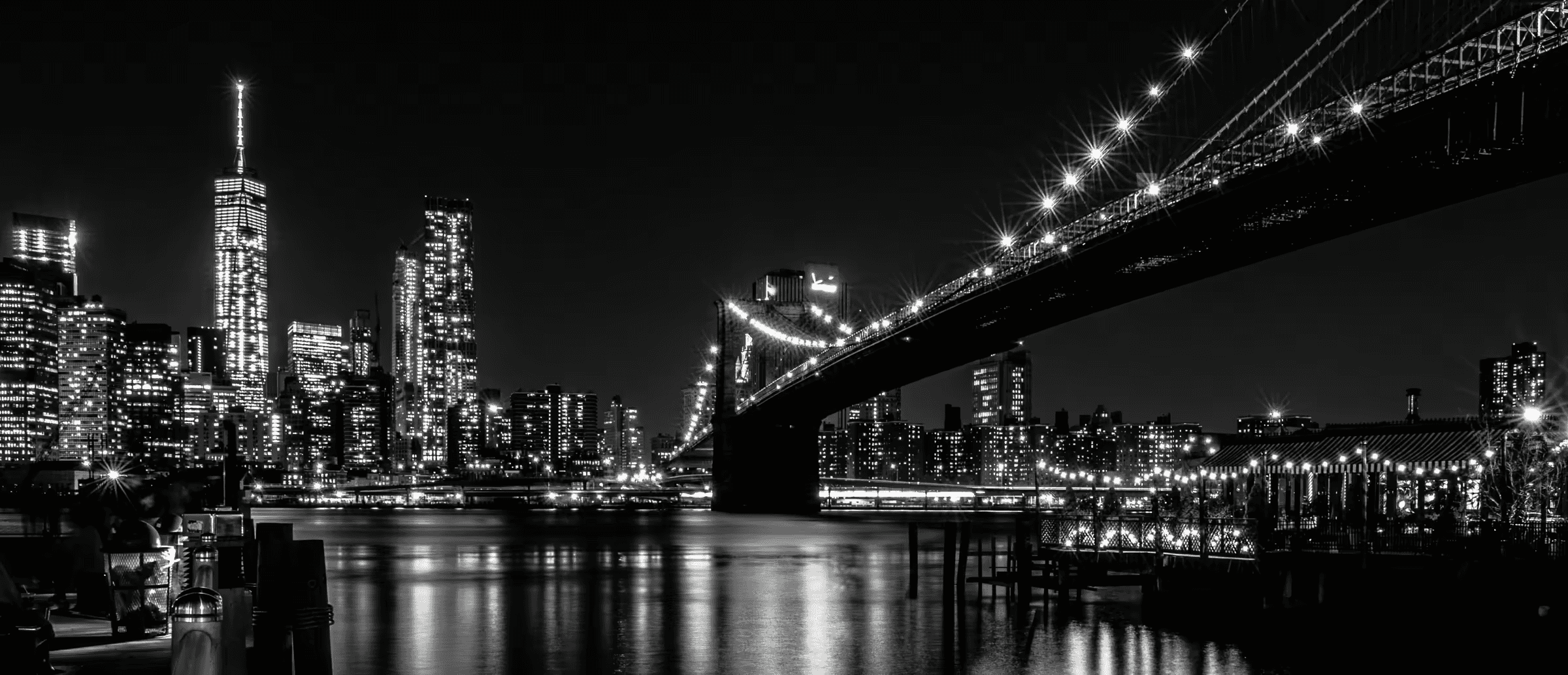 Monochrome cityscape featuring the Brooklyn Bridge's Gothic Revival architecture illuminated against the Manhattan skyline.