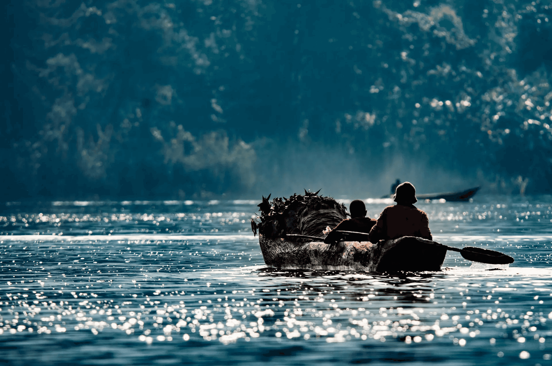 A scenic photograph of a traditional dugout canoe-style boat gliding across the sparkling waters of Lake Bunyonyi in Uganda.
