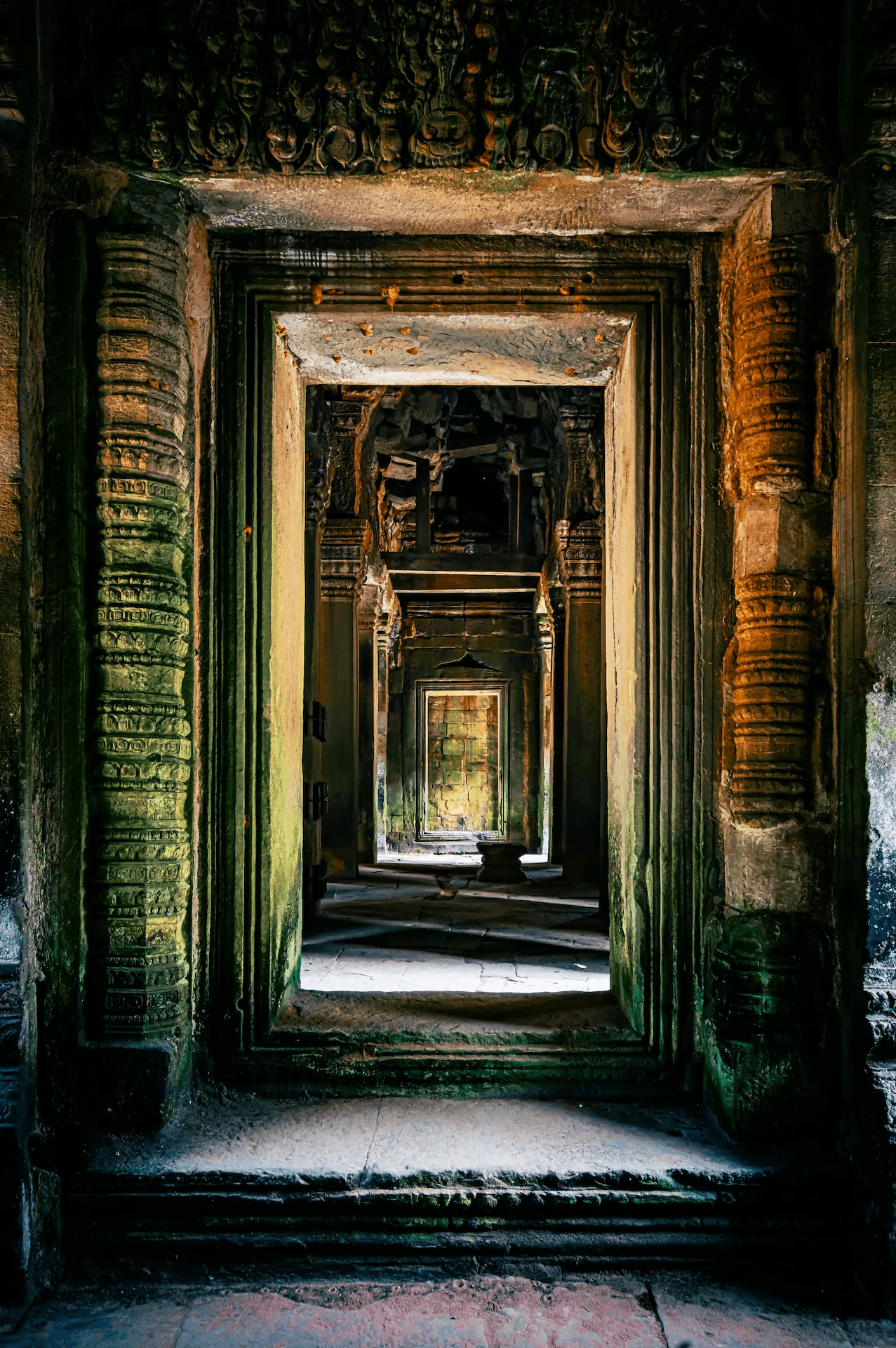 Stone corridor in Ta Nei Temple, Angkor, Cambodia. The photograph showcases a long passageway framed by ancient stone doorways and columns, with light filtering from the distant end. The weathered textures of the Khmer architecture and the play of light and shadow are prominent. Evocative image of ancient temple ruins in Southeast Asia.