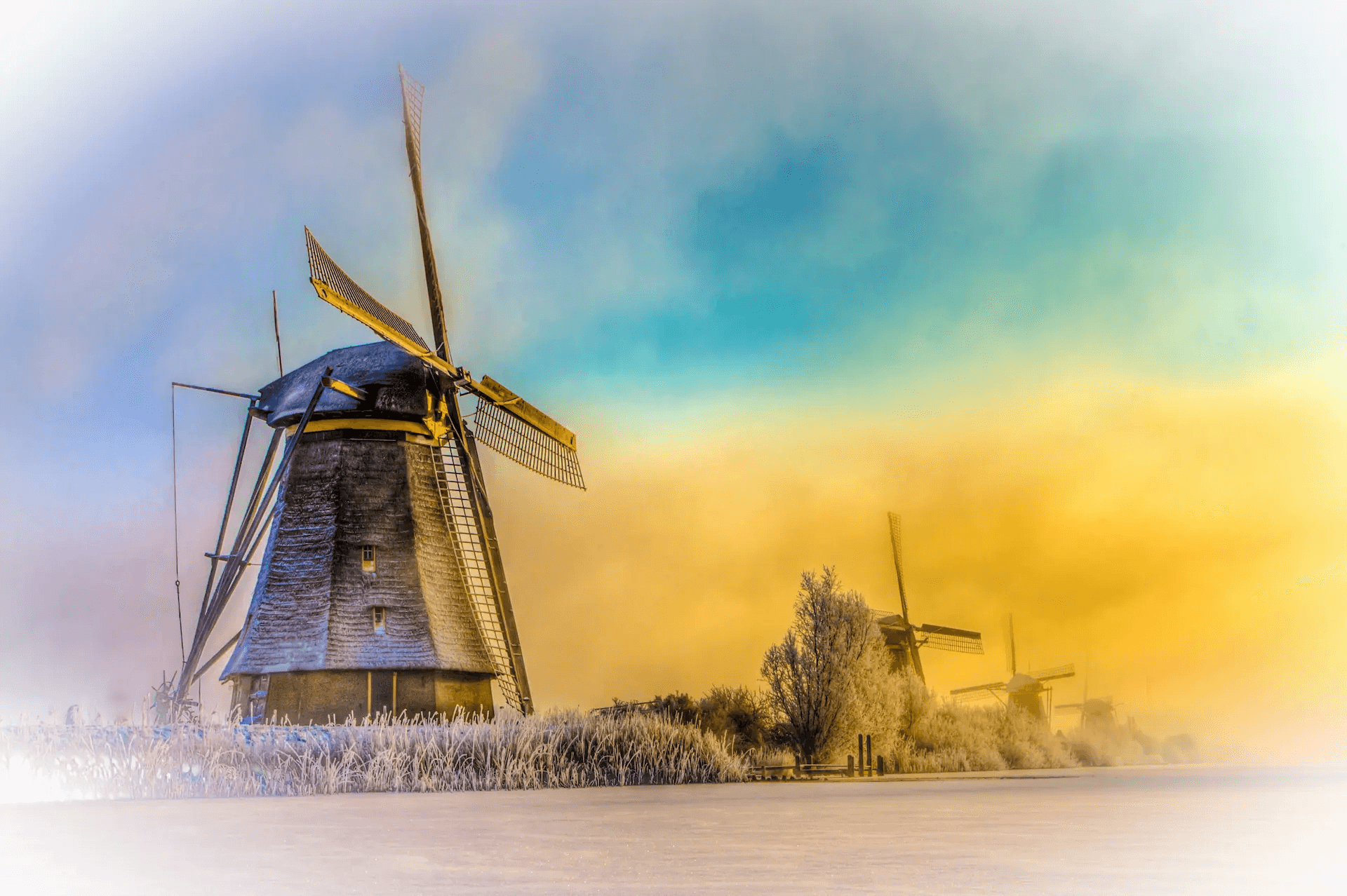 A picturesque winter landscape photograph of the windmills at Kinderdijk, Netherlands.  Several traditional windmills stand prominently against a pastel-colored sky, ranging from soft blues to warm yellows.