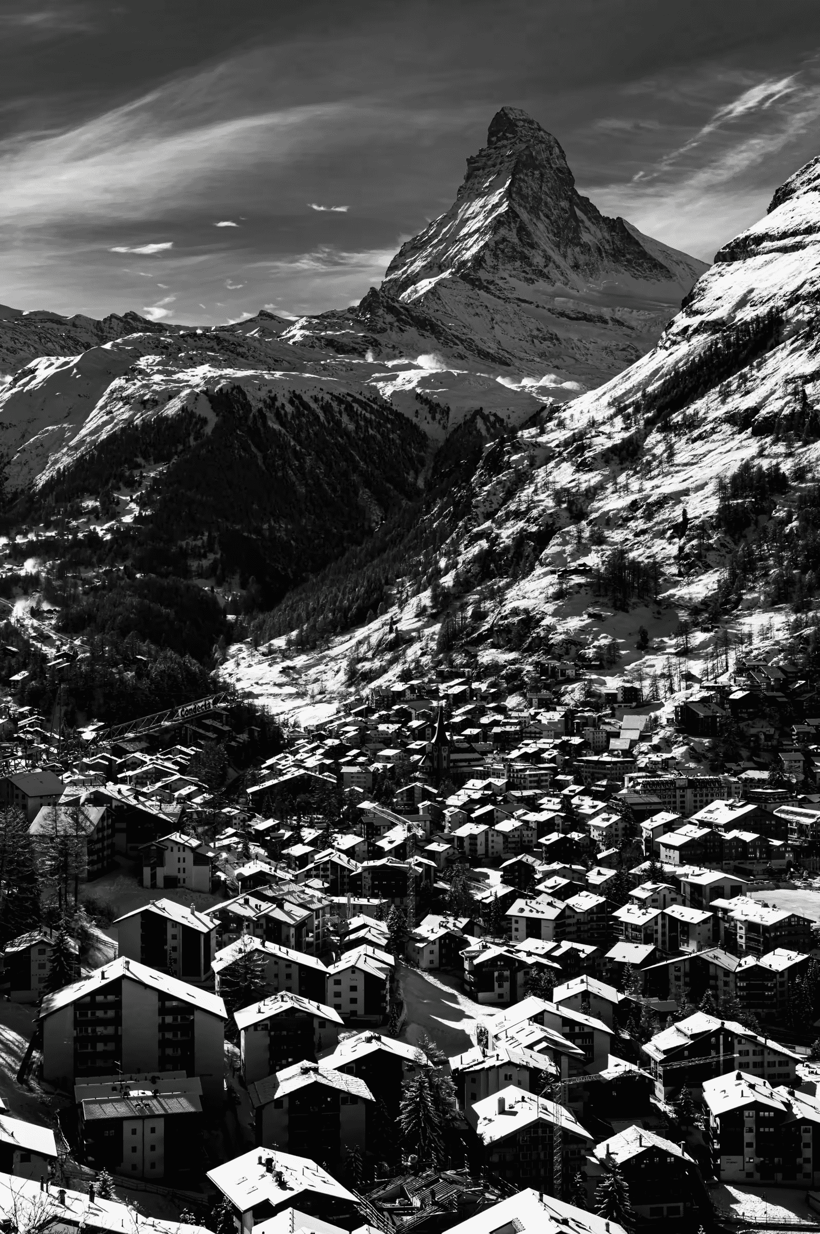 High-contrast, black and white photograph of the snow-covered village of Zermatt, with the iconic Matterhorn mountain in the background.
