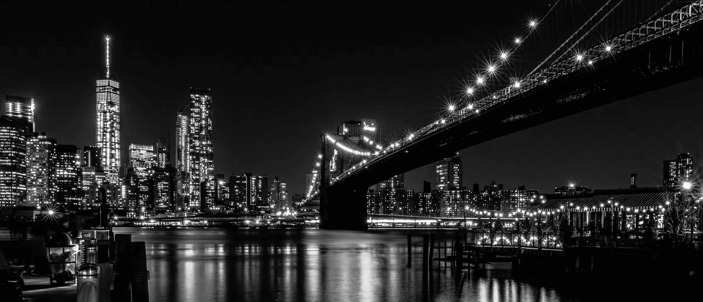 Brooklyn Bridge: Urban Nocturne Monochrome cityscape featuring the Brooklyn Bridge's Gothic Revival architecture illuminated against the Manhattan skyline.