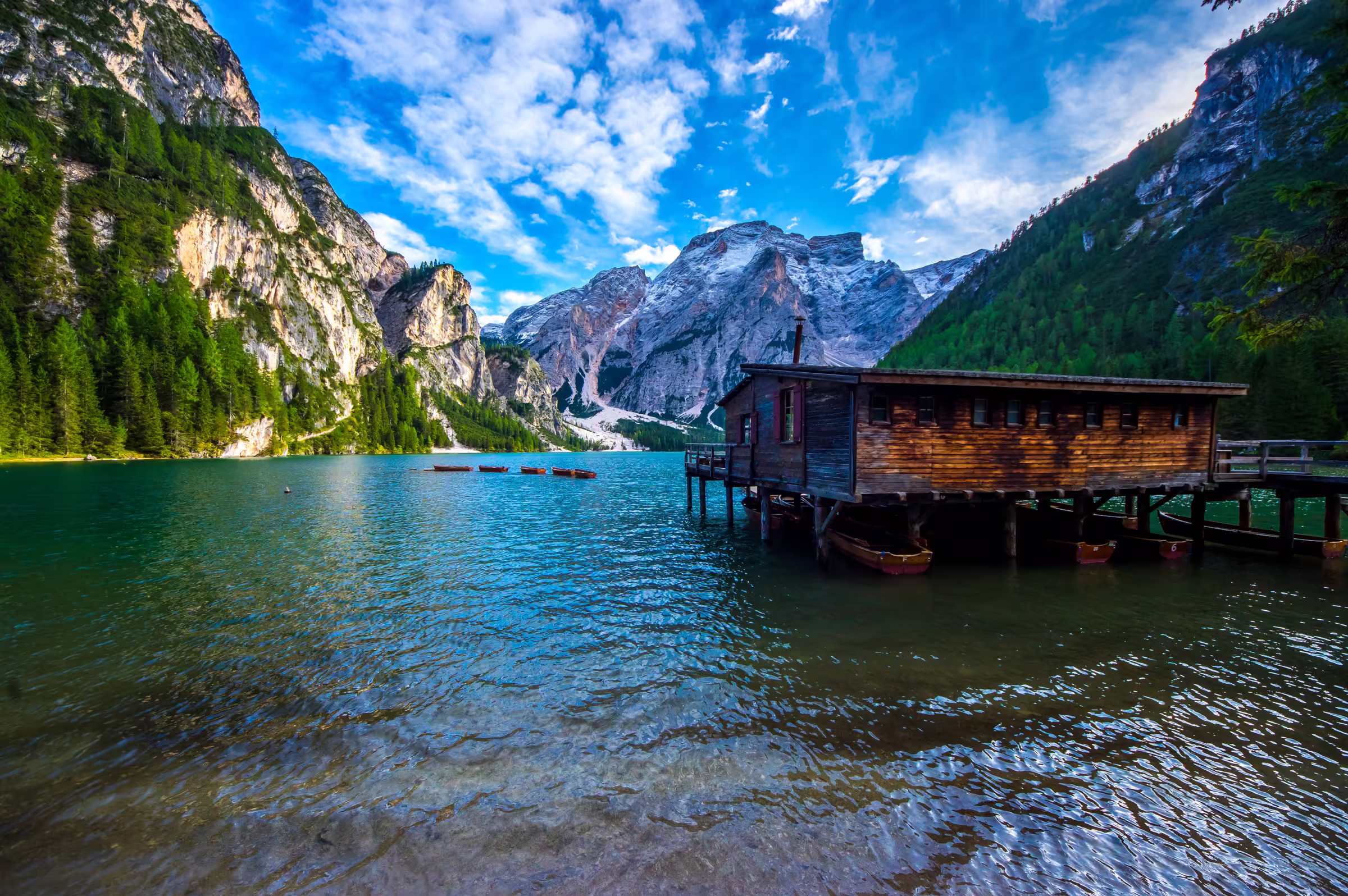 Landscape photograph of Lago di Braies (Pragser Wildsee) in the Dolomites, Italy. A wooden boathouse sits on the edge of the turquoise lake.