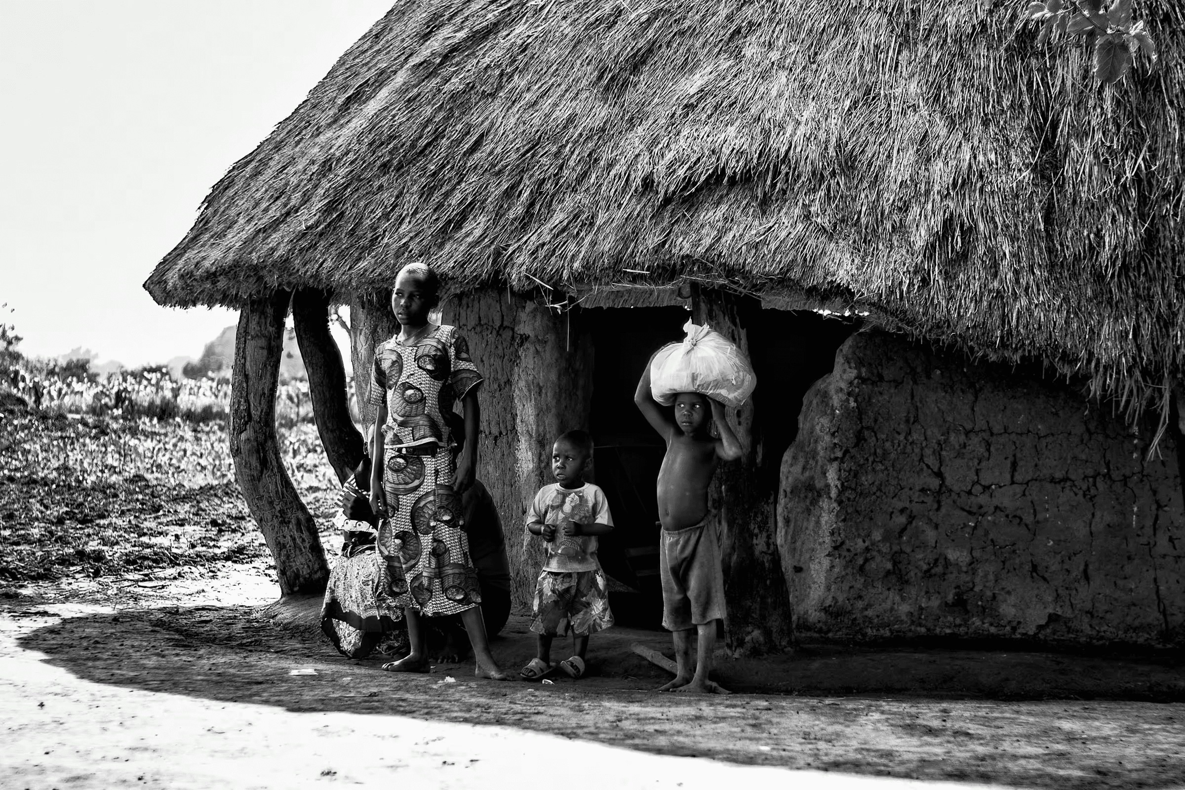 A Ugandan family standing outside their traditional mud hut with a thatched roof.