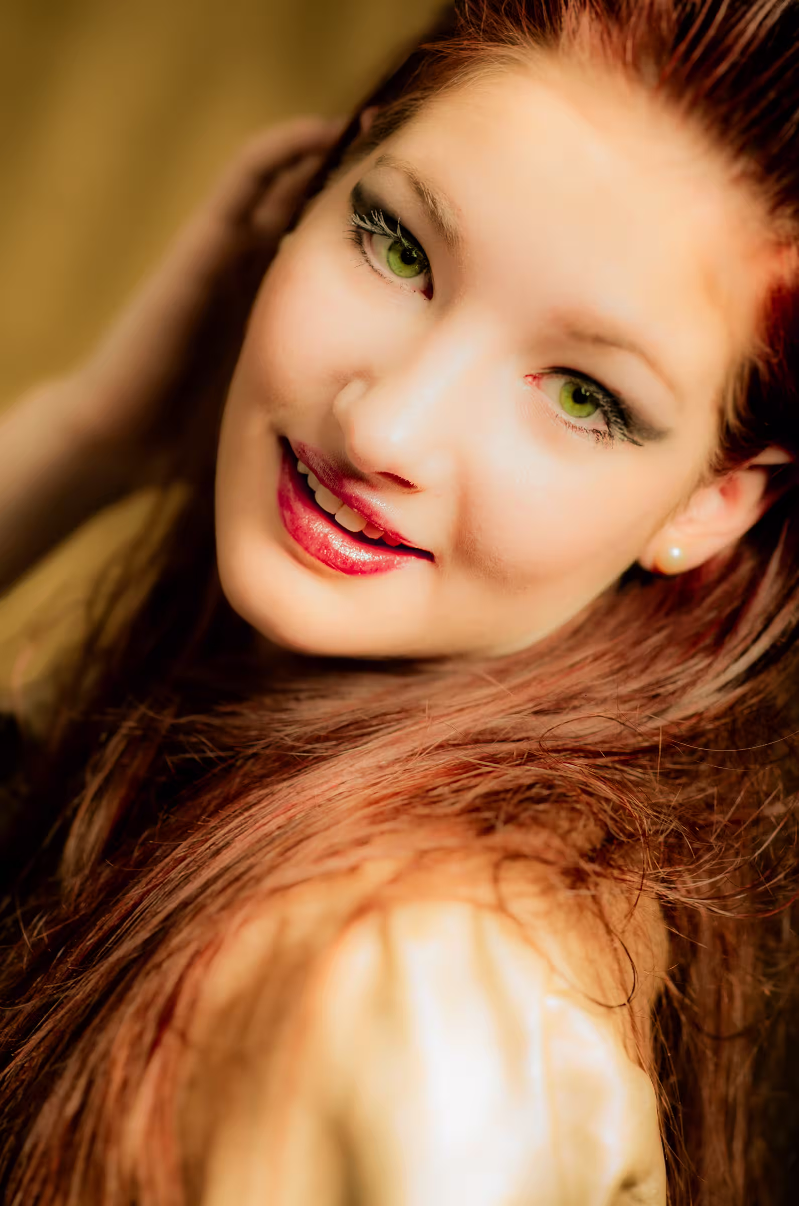 Portrait of a young woman with long, flowing auburn hair and striking green eyes. She is smiling slightly and looking towards the camera.
