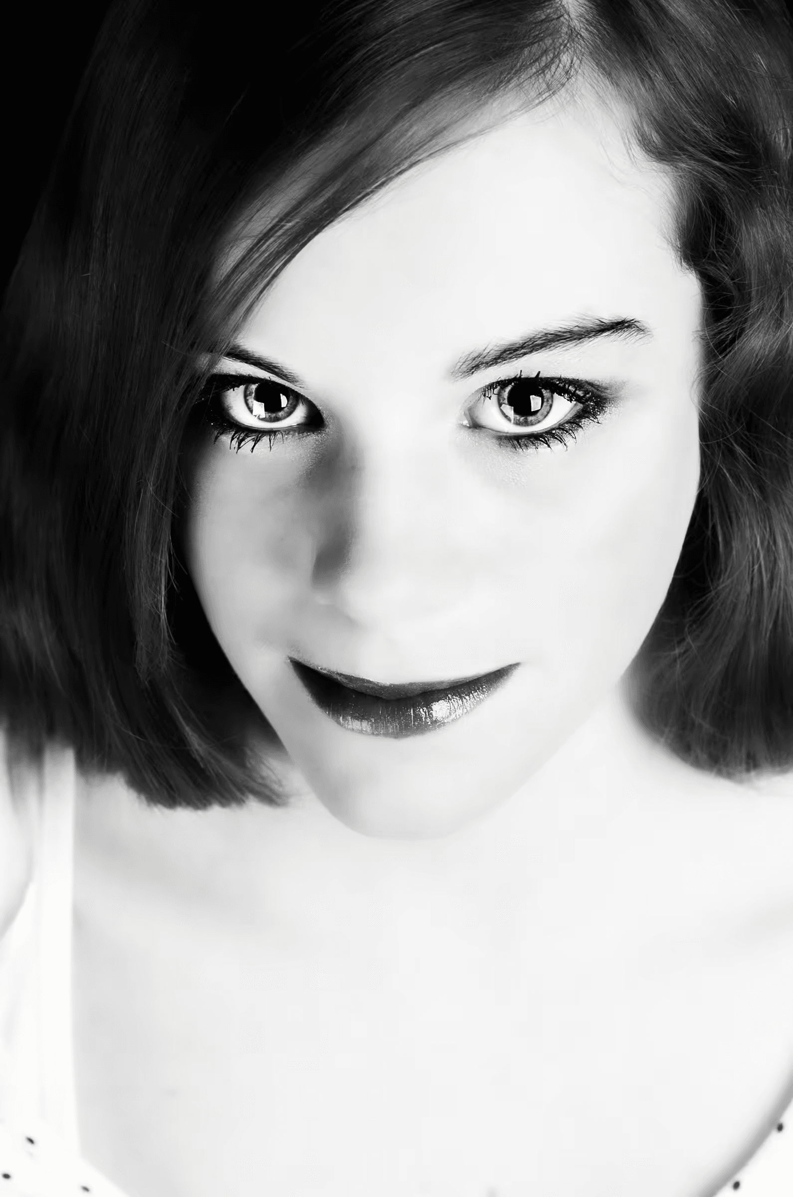 Monochrome portrait photograph of a woman with a direct and intense gaze. The woman is framed from a slightly high angle, emphasizing her eyes and facial expression.  The image is rendered in black and white, highlighting the contrast and light.  Evocative portraiture, woman, intense gaze, monochrome, black and white.